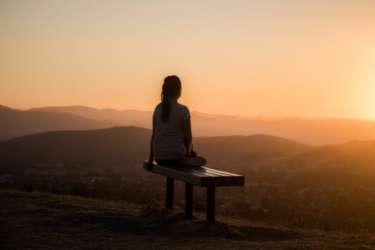 Overexcitabilities und hochbegabung können einsam machen: Frau sitzt alleine auf einer Bank und schaut sich den Sonnenuntergang an